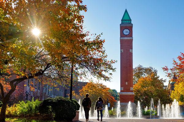 Two students walking next to 博彩网址大全's clock tower on a spring day